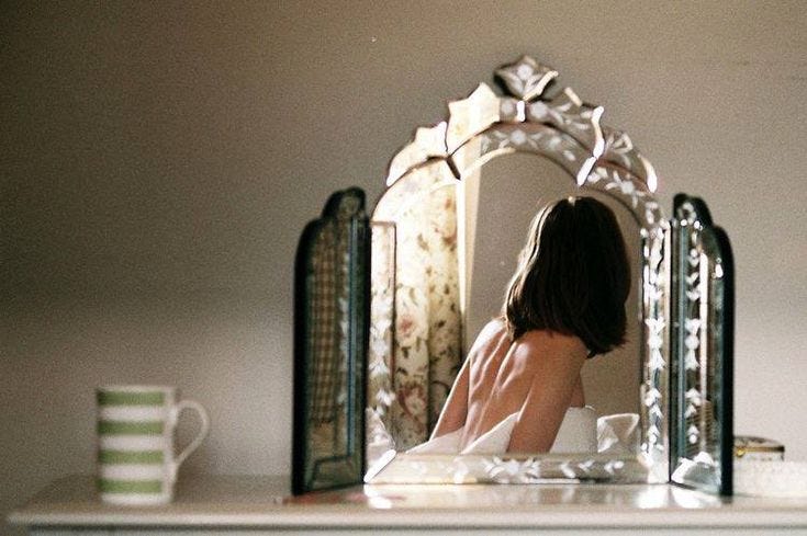 This may contain: a woman sitting in front of a mirror on top of a dresser next to a cup This may contain: a woman sitting in front of a mirror on top of a dresser next to a cup