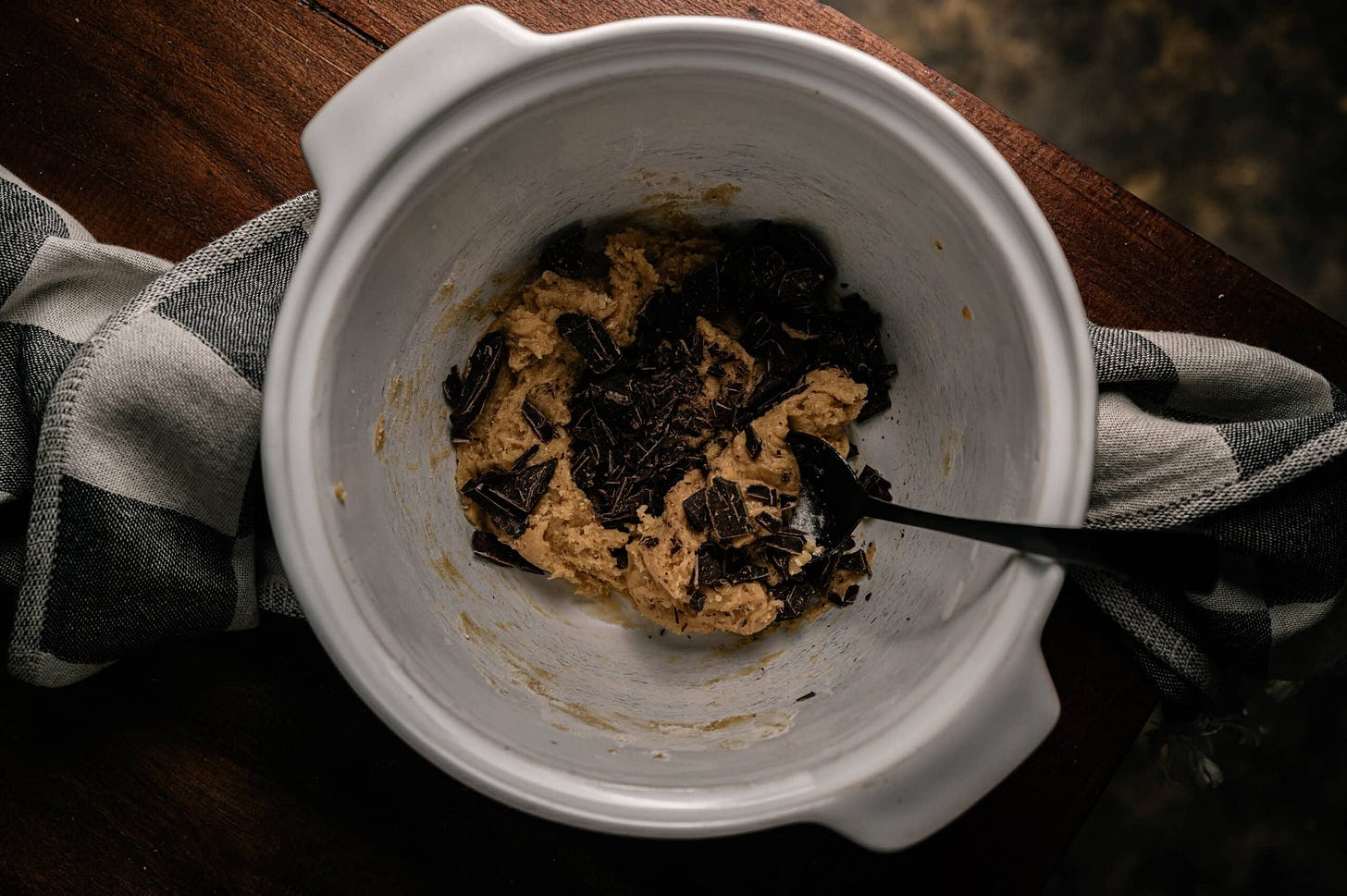 folded dough with chocolate in a white bowl on a brown table. 