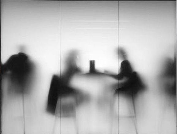 This may contain: black and white photograph of people sitting at a table in front of glass partitions