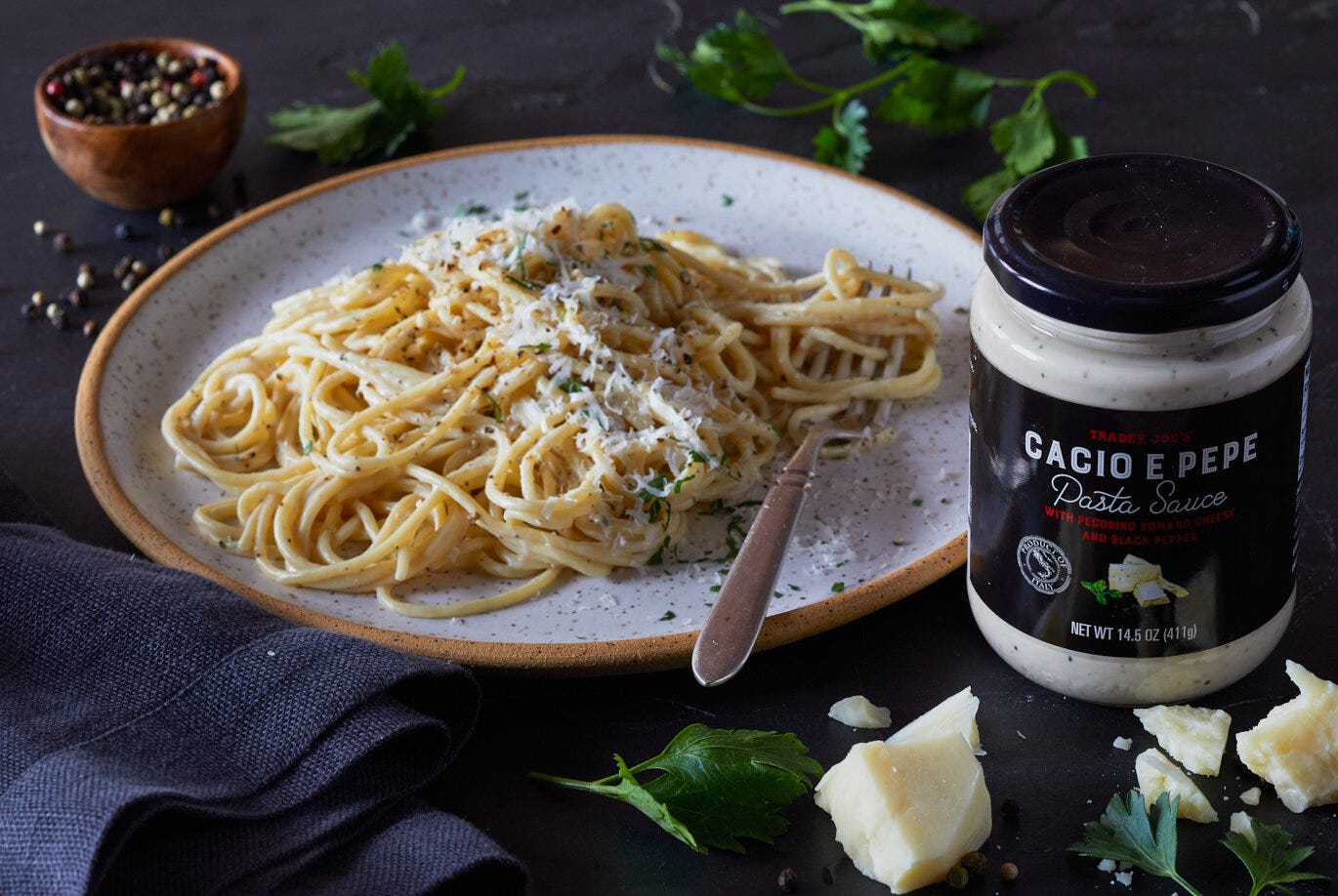 Trader Joe's Cacio e Pepe Pasta Sauce packaging next to a plate of cacio e pepe spaghetti garnished with pepper, parsley and shredded parmesan