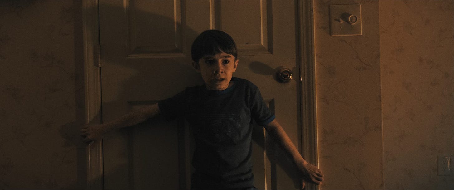 Alex (Cary Christopher) tries to keep a door barricaded in Weapons. Alex (Cary Christopher) tries to keep a door barricaded in Weapons.