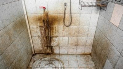 Image of a very dirty shower stall with red/brown and black filth encrusting the floor and extending several feet up the walls. Image of a very dirty shower stall with red/brown and black filth encrusting the floor and extending several feet up the walls.