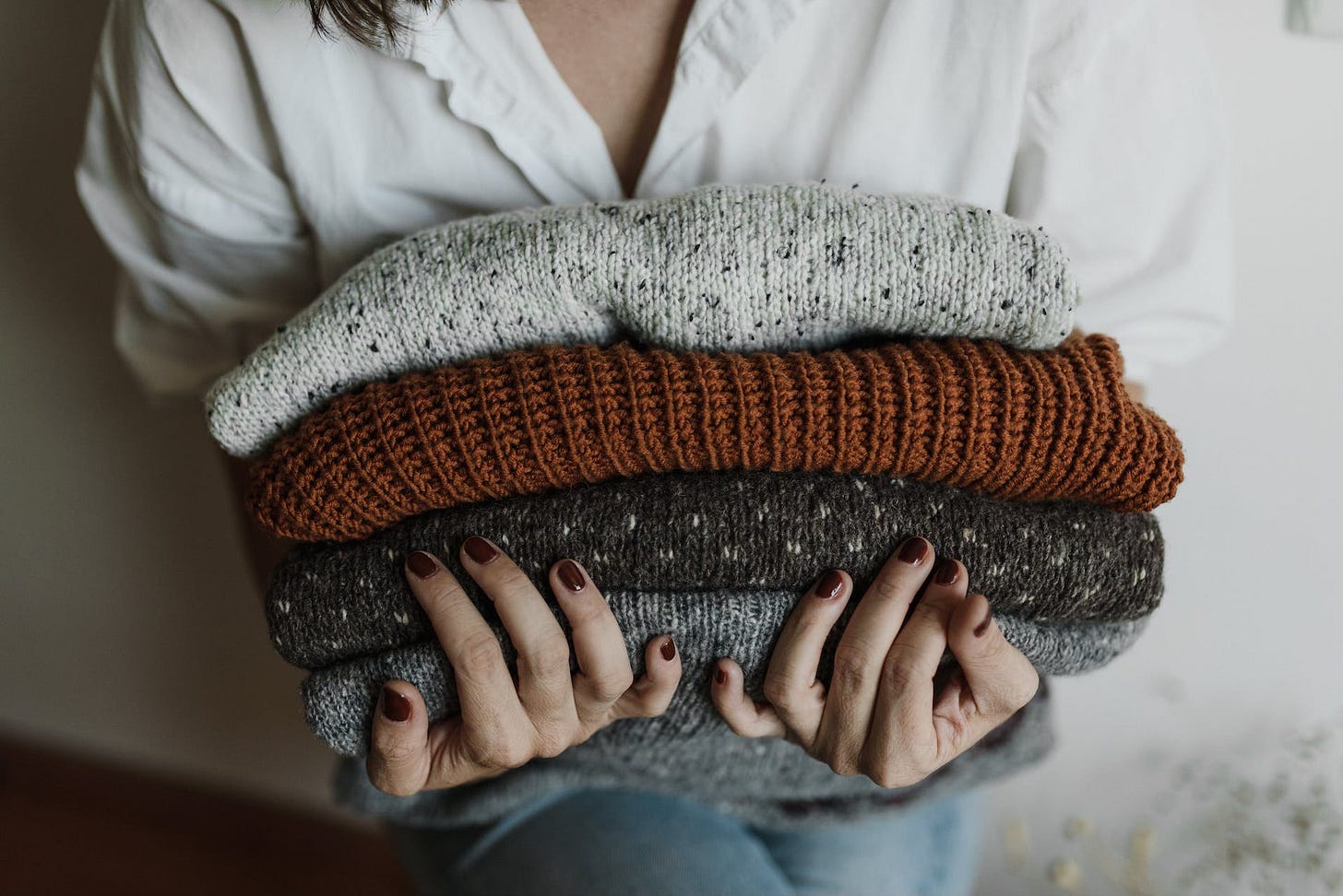 A woman holds four neatly folded sweaters in her arms