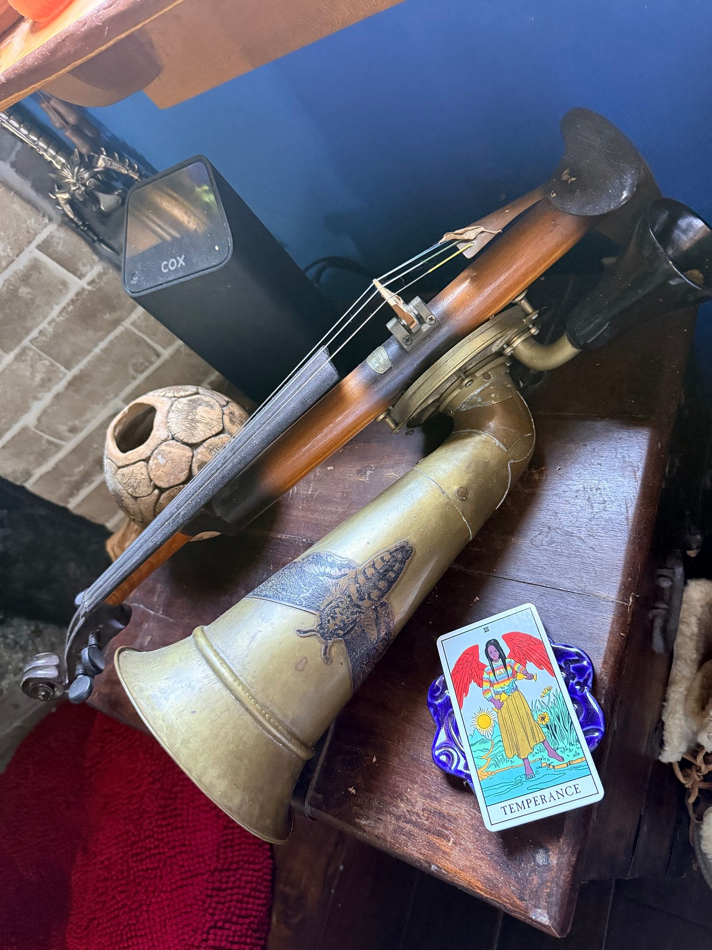 A vintage Stroh violin with a large brass amplifying horn rests on a wooden table beside the Temperance tarot card. A vintage Stroh violin with a large brass amplifying horn rests on a wooden table beside the Temperance tarot card.