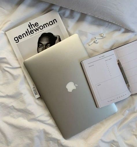 This may contain: an apple laptop computer sitting on top of a bed next to a notepad and pen