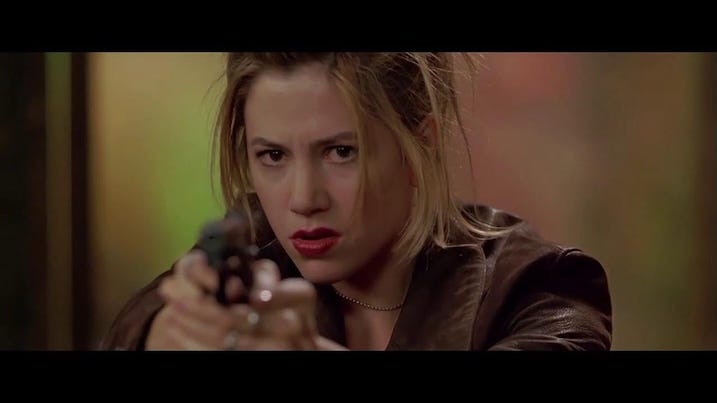 Mira Sorvino aiming a handgun with a focused expression in a tense moment from The Replacement Killers.