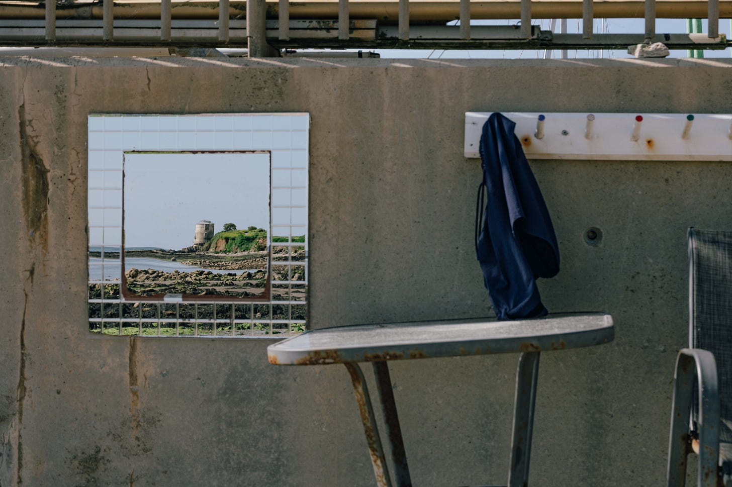 A seaside view framed through a square mirror mounted on a concrete wall, reflecting a Martello tower along the Dublin coast. A seaside view framed through a square mirror mounted on a concrete wall, reflecting a Martello tower along the Dublin coast.