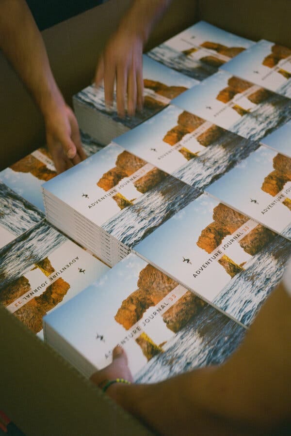 A large box of issues of Adventure Journal. Hands can be seen at the top of the frame, packing the box.
