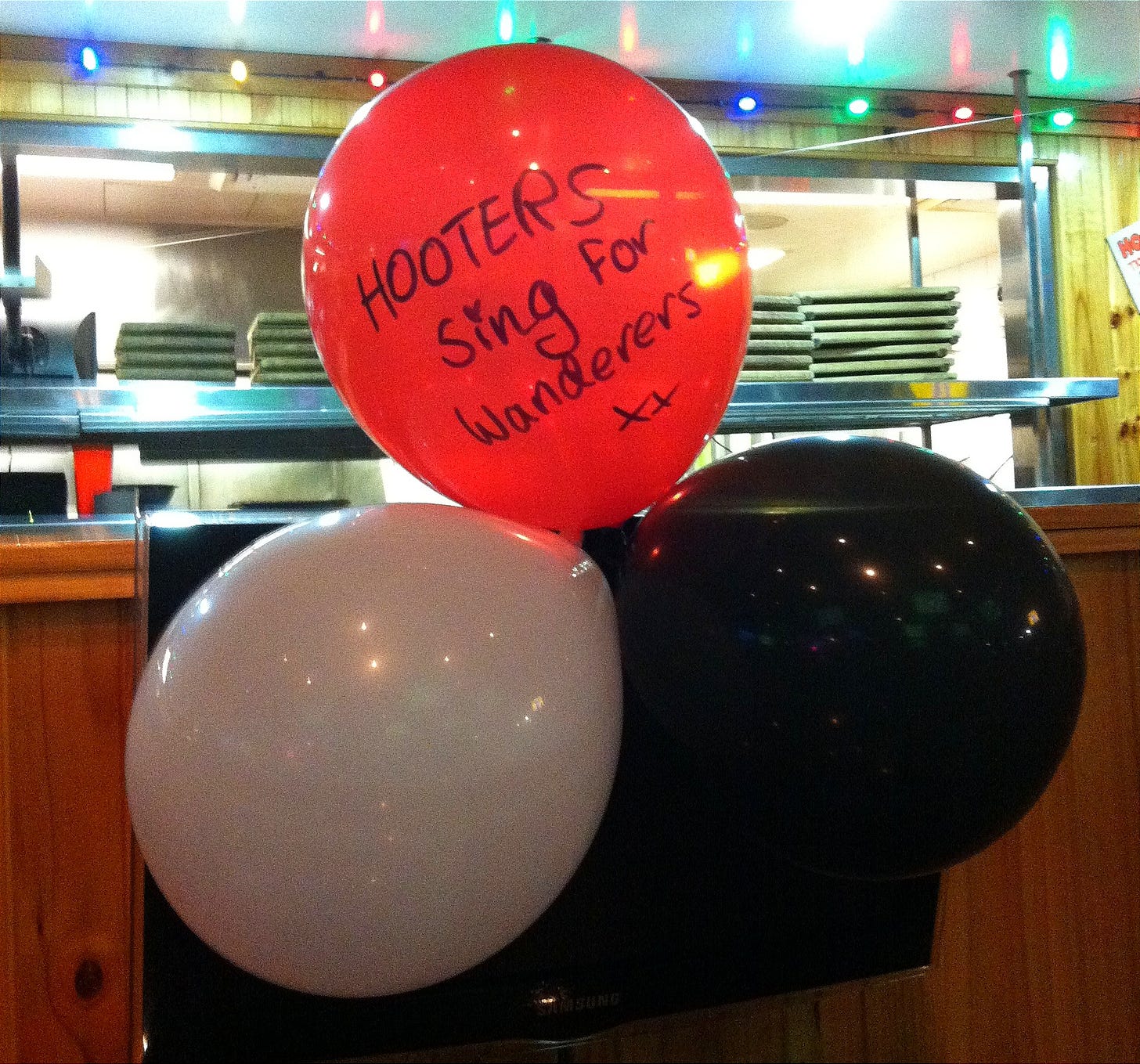 Red, black and white balloons with a message reading 'Hooters sings for Wanderers'