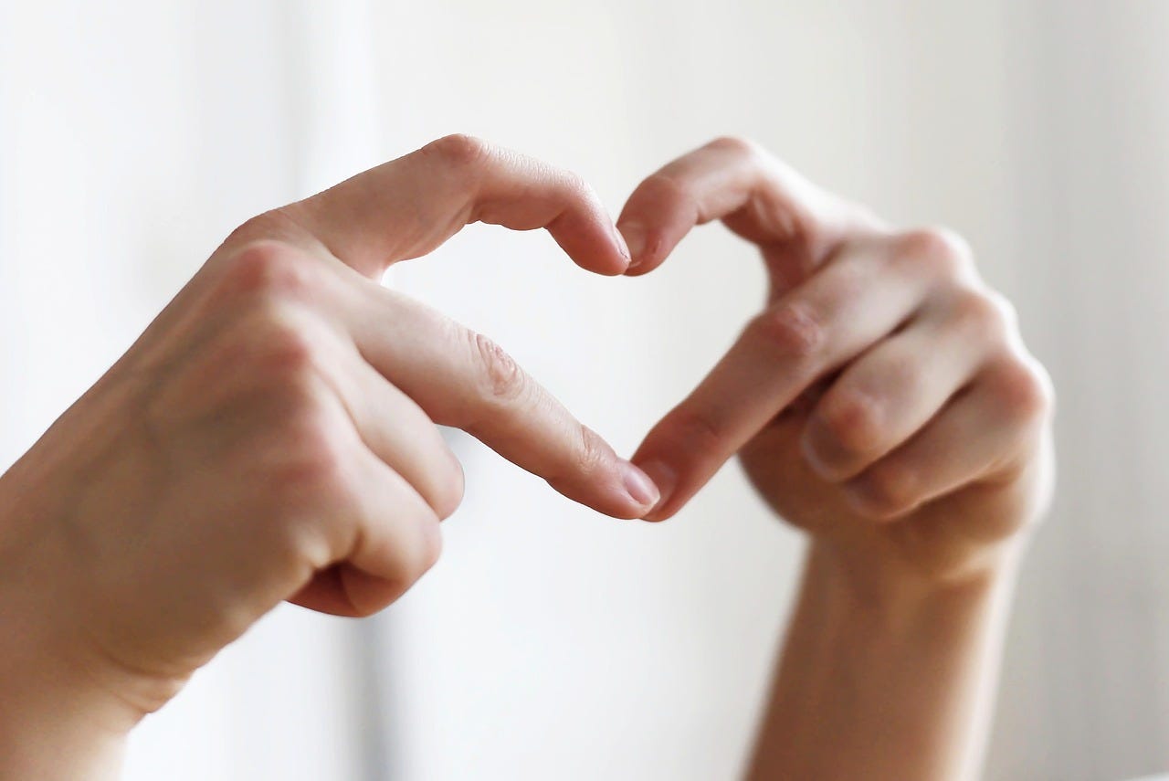 Two hands come together to make a heart shape with fingers