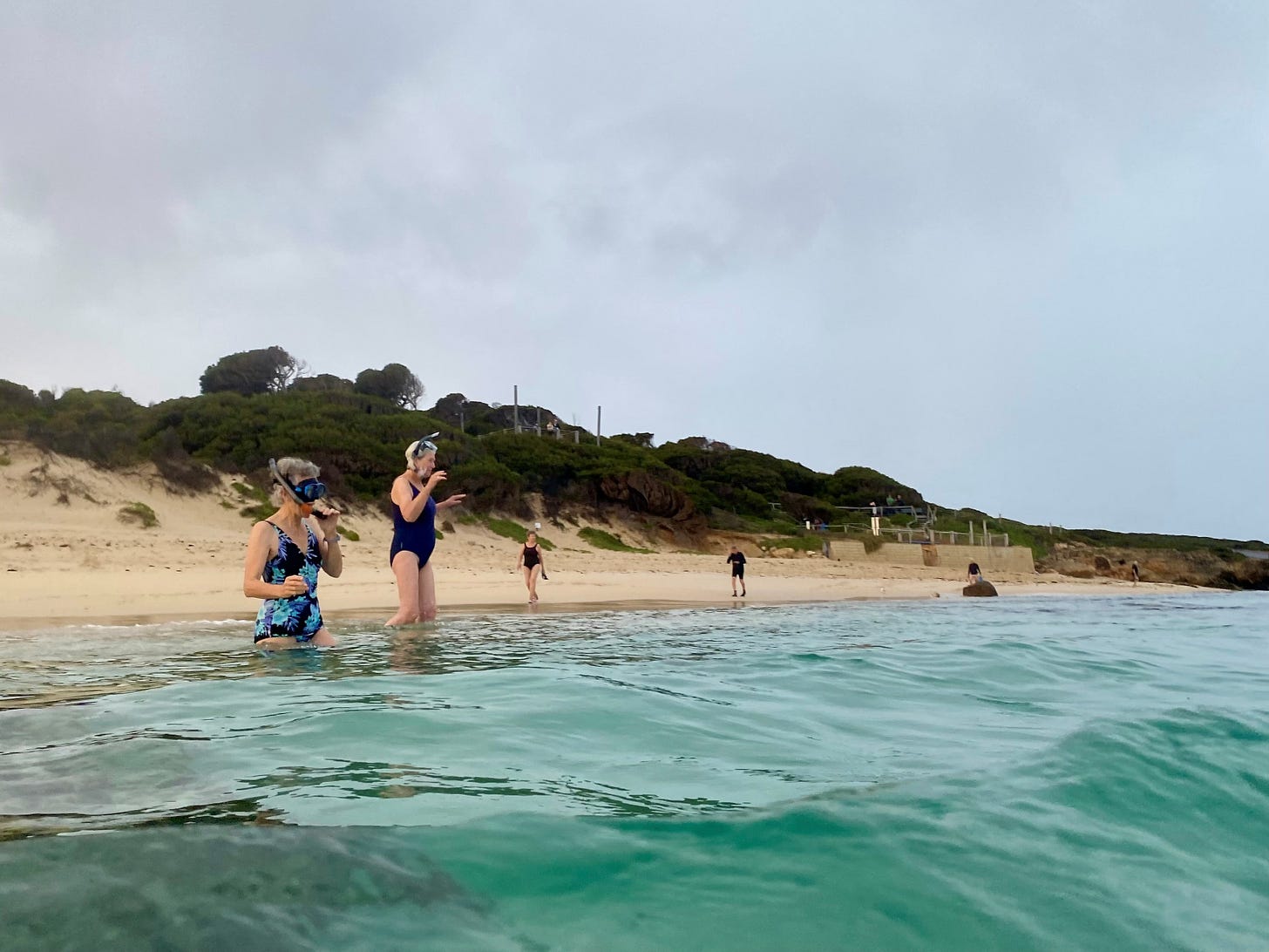 People stand on the shore, preparing to dive into the ocean for a swim
