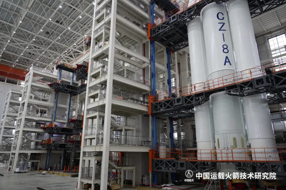 A Long March 8A first-stage and boosters being worked on inside a preparation bay (closest to the camera) while another awaits a launch vehicle (at distance on the right side).