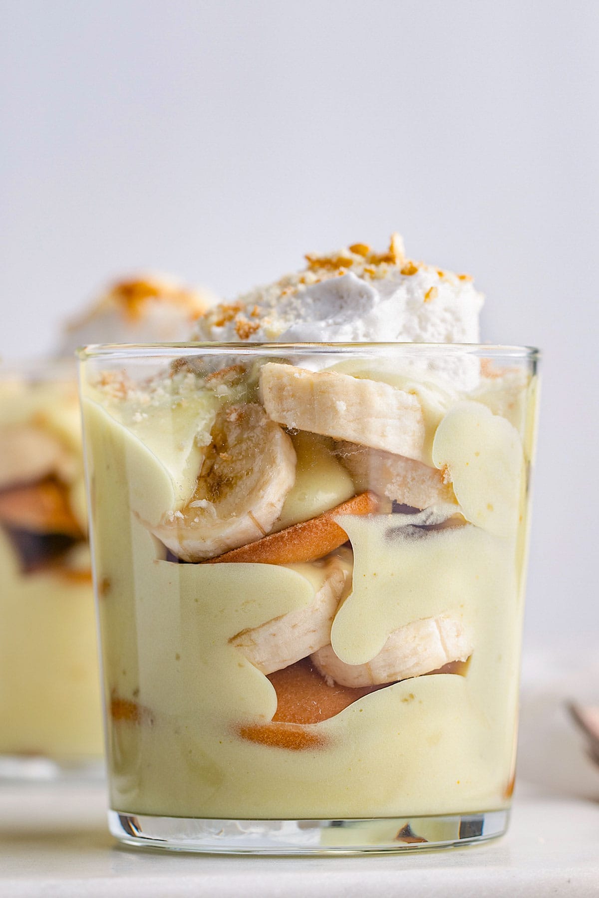 Side view of a short glass holding vegan banana pudding layered with slices of bananas and Nilla wafers. Side view of a short glass holding vegan banana pudding layered with slices of bananas and Nilla wafers.