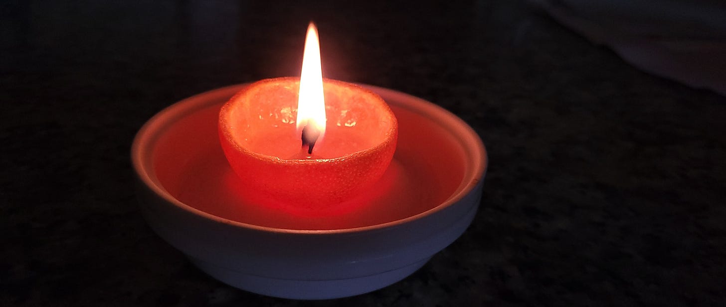 An oil lamp made from half a mandarin orange peel. It is burning brightly.