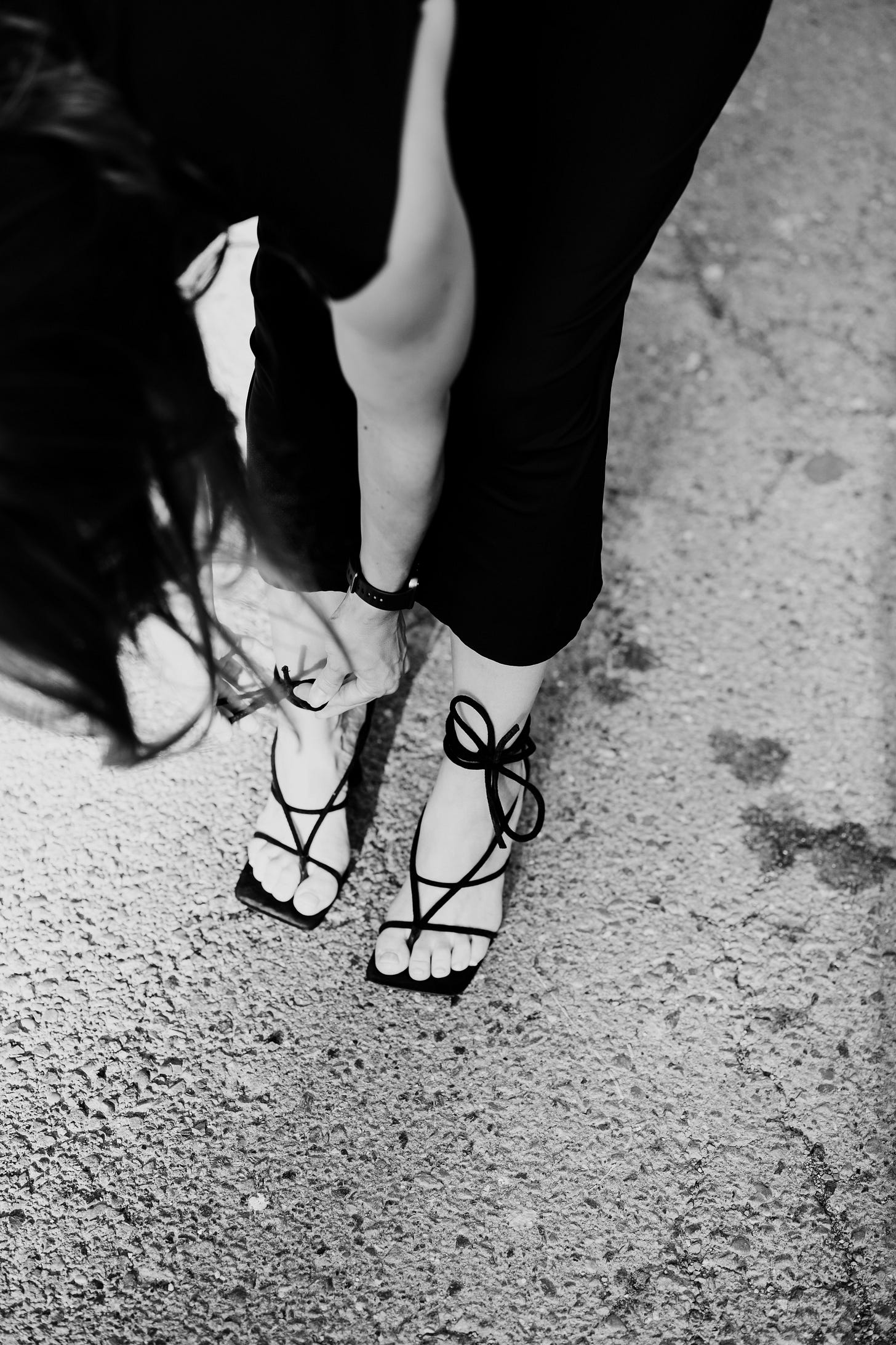 woman in a long black dress leans down to fasten her high heel sandals.