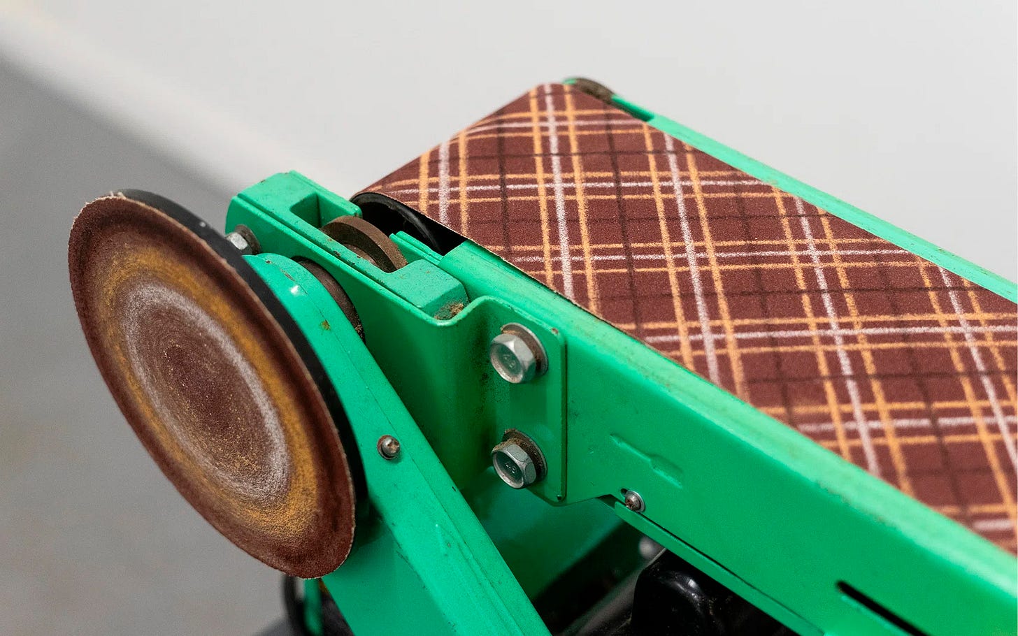 Close-up of a green vintage sanding machine with plaid drawing on sandpaper and spinning circular wheel. Close-up of a green vintage sanding machine with plaid drawing on sandpaper and spinning circular wheel.