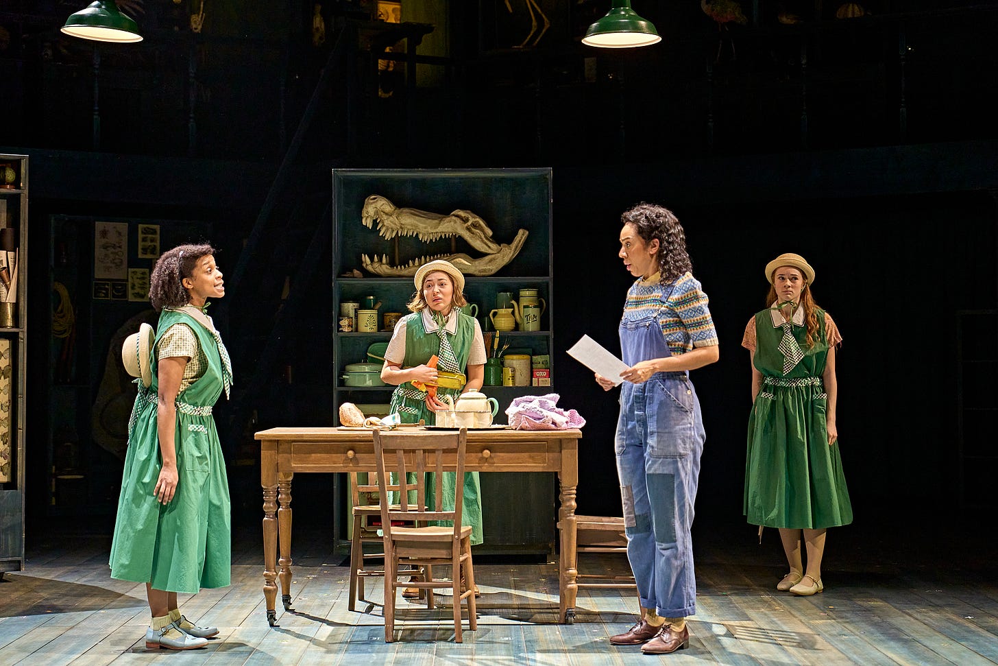 A photograph showing the three Fossil sisters in green school uniforms and Sylvia in a kitchen from Ballet Shoes A photograph showing the three Fossil sisters in green school uniforms and Sylvia in a kitchen from Ballet Shoes