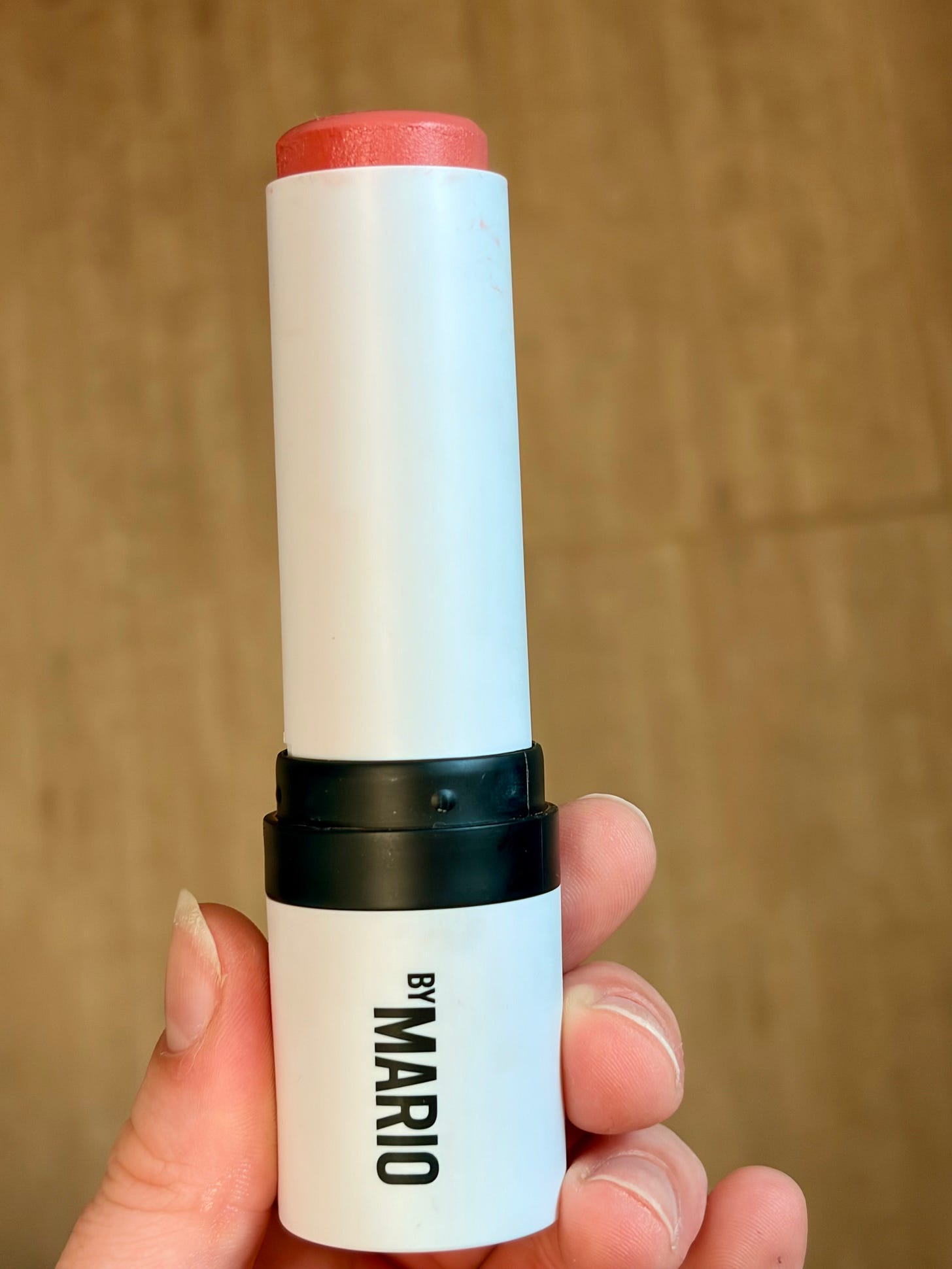 A sleek Makeup By Mario Soft Pop Blush Stick with the creamy, pink blush product rolled up slightly against a minimalist backdrop.