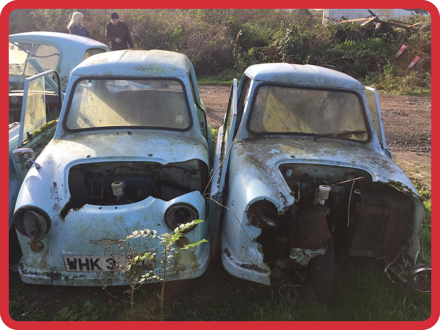 A photo of two partially destroyed blue invalid carriages in a field. Their bonnets have been badly damaged, so inside we can see their broken, rusting engines. A photo of two partially destroyed blue invalid carriages in a field. Their bonnets have been badly damaged, so inside we can see their broken, rusting engines.