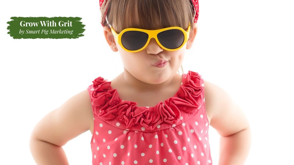 A young child wearing oversized yellow sunglasses and a bright pink polka-dot outfit stands with hands on hips and a playful, confident expression against a white background. The image symbolizes individuality, authenticity, and developing a distinctive personality instead of blending in. Grow With Grit by Smart Pig Marketing branding appears in the upper left corner.
