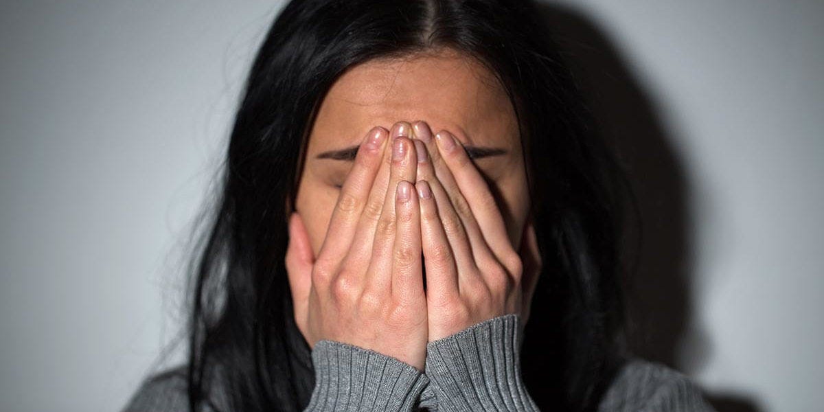 a woman holding her hands in front of her face, clearly struggling, thinking about the early warning signs of her abusive relationship