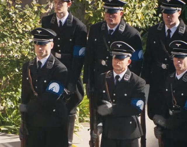Image one: a room with blue Paramount flags draping down the windows, and a man dressed like a WWII Nazi. Image 2: Paramount's security forces wearing the Paramount logo in place of a Swastika armband.