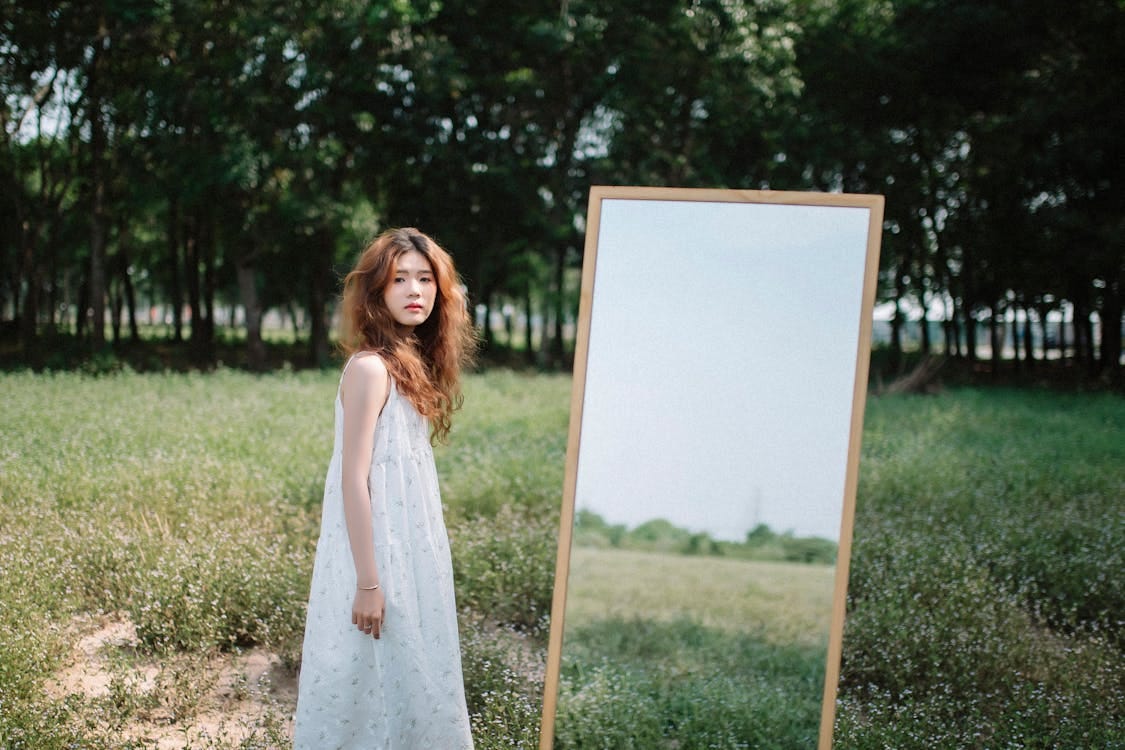 Free A young woman stands in a serene park, reflecting in a mirror under summer trees. Stock Photo
