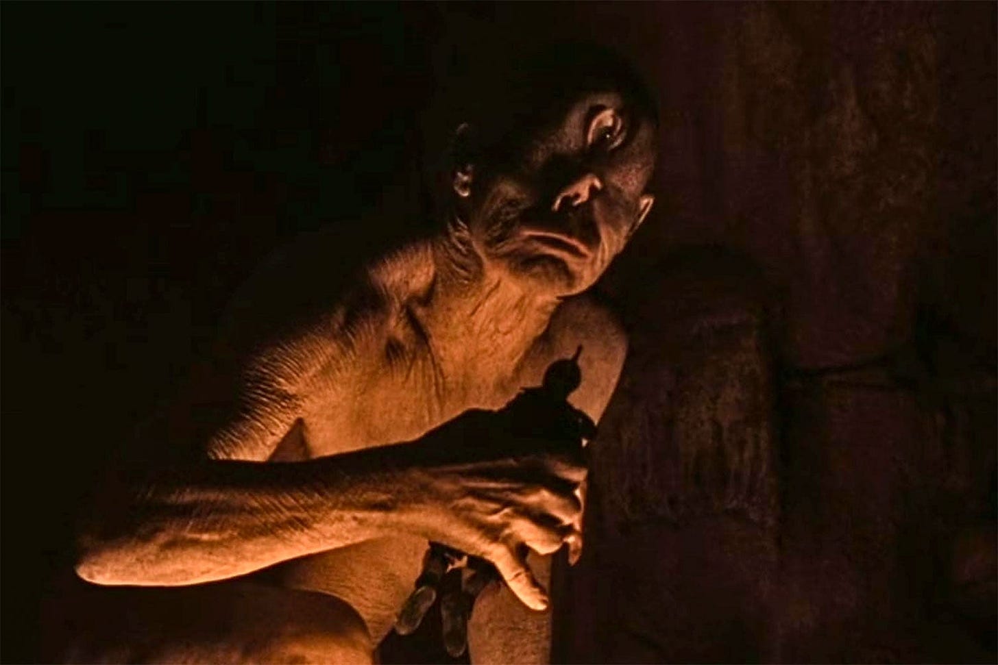 A still shows a very human looking figure, except with wrinkly skin and a single eye, turned to the side on his forehead, leaning forward into the light cast by a fire, the silhouette of a Greek soldier in his hands.
