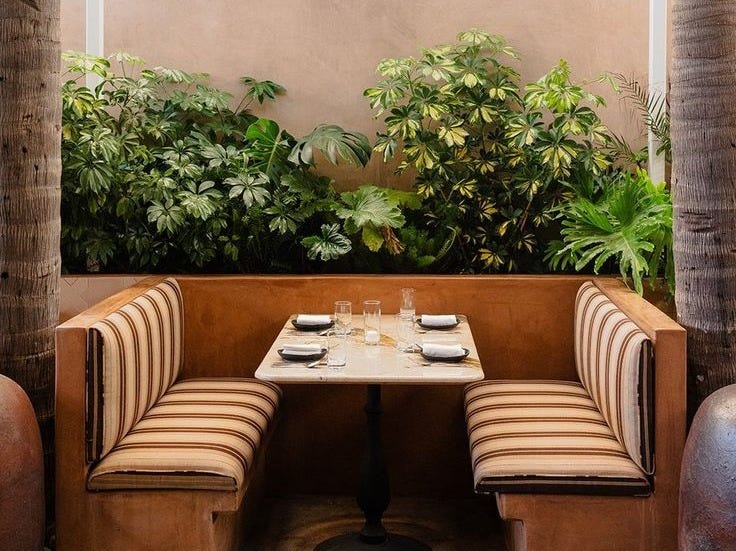 This may contain: a table and two benches in a room with plants on the wall behind it, surrounded by tall palm trees