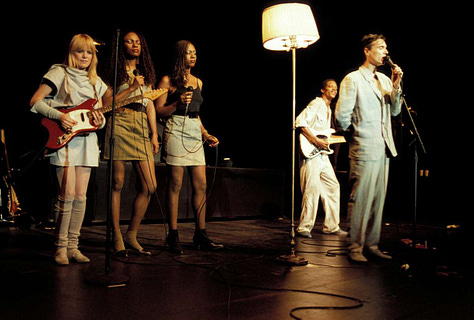 selects from Talking Heads' concert film Stop Making Sense. images of Byrne holding a microphone to camera, raising his arms, dancing in a big suit an with a lamp and full shots of the band.