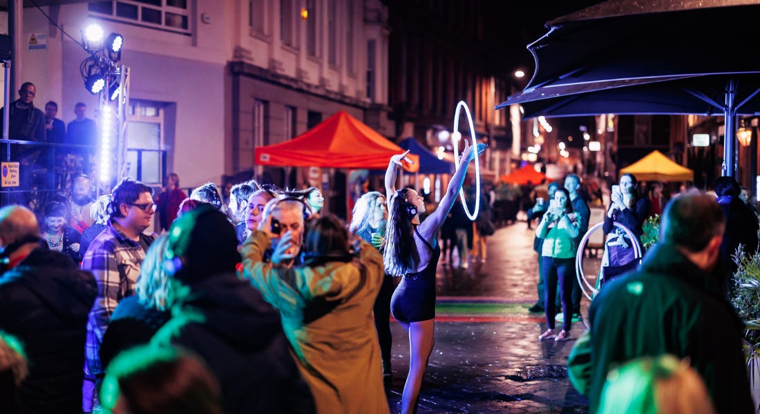 A crowd of people on a street with a girl holding an illuminated hoop A crowd of people on a street with a girl holding an illuminated hoop