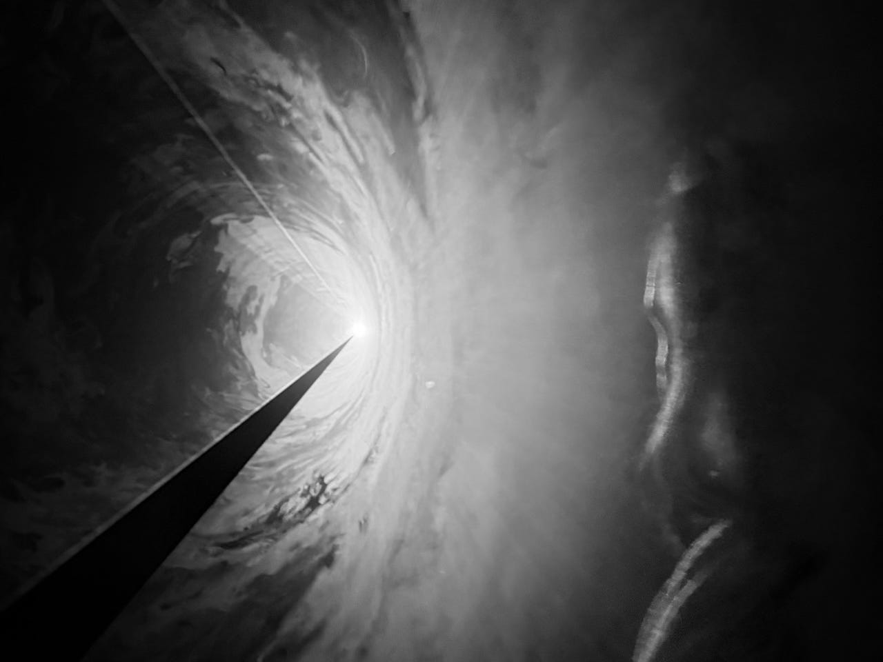 GPT-4o: Black and white photograph capturing a mist-filled room where a bright light source illuminates a conical surface of mist. The cone is incomplete, as an obstruction near the light source casts a sharp shadow, creating a dark wedge that interrupts the illuminated area. A faint, linear streak extends parallel to the shadow. On the right side, a ghostly human-like face emerges from the mist, partially veiled by the swirling light and darkness, adding an ethereal and mysterious quality to the scene. GPT-4o: Black and white photograph capturing a mist-filled room where a bright light source illuminates a conical surface of mist. The cone is incomplete, as an obstruction near the light source casts a sharp shadow, creating a dark wedge that interrupts the illuminated area. A faint, linear streak extends parallel to the shadow. On the right side, a ghostly human-like face emerges from the mist, partially veiled by the swirling light and darkness, adding an ethereal and mysterious quality to the scene.