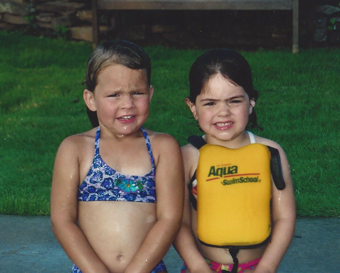 Two preschool-aged girls in swimsuits standing side by side after a dip in the pool