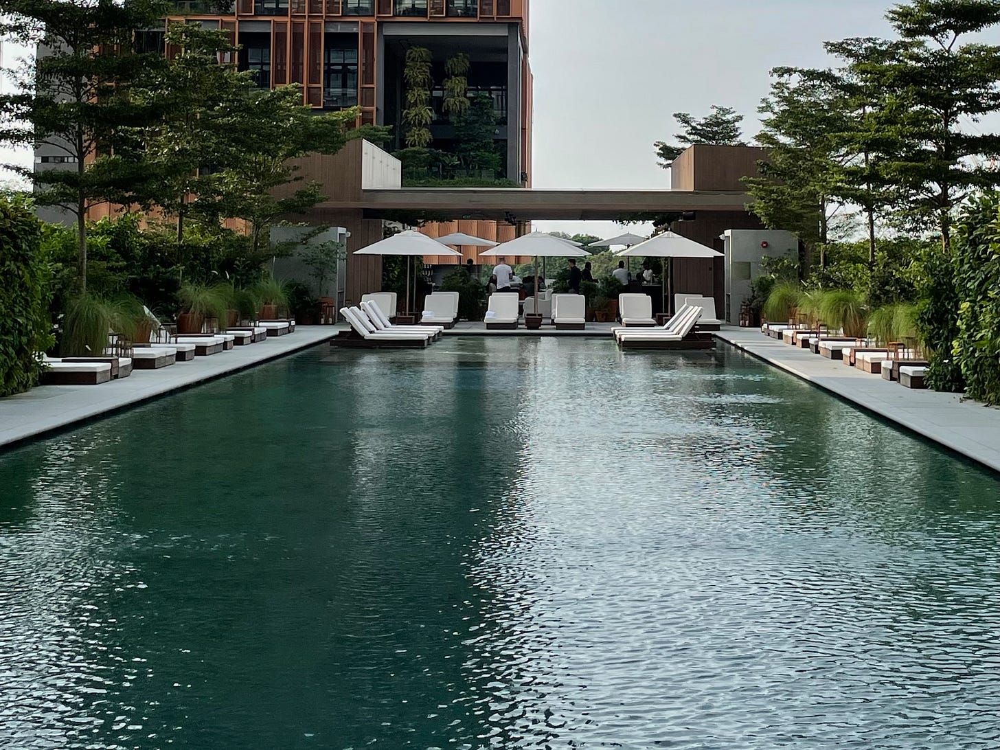 A swimming pool is shown atop a bridge that spans a courtyard between an apartment building and a hotel.