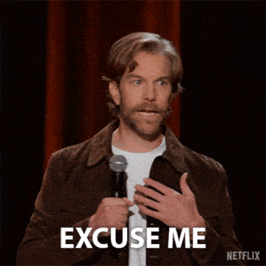 a man with a beard is holding a microphone and says but what the fuck is this