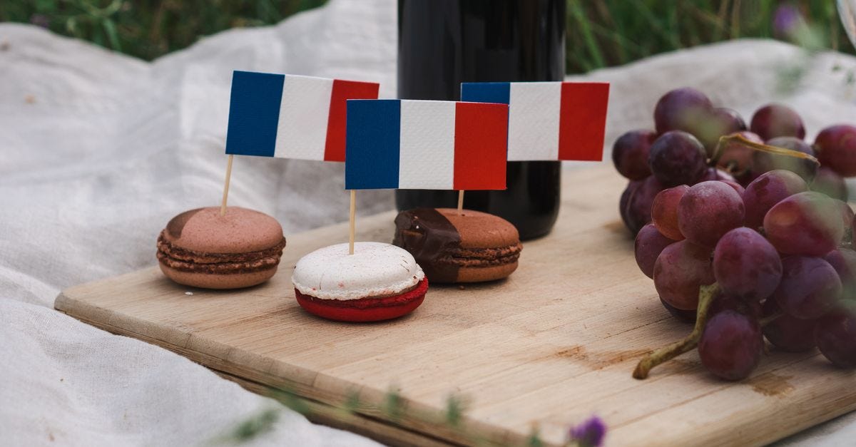 Photo: Polina ⠀ / Pexels Macarons decorated with French flags on a picnic setup with grapes and wine.