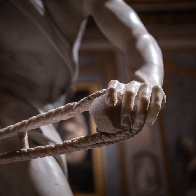 The image is a detailed close-up of the hand of the sculpture 'David' by Gian Lorenzo Bernini. The hand is intricately carved, showing a firm grip on a sling, which is a key element of the biblical story of David and Goliath. The texture of the marble is beautifully rendered, highlighting Bernini's mastery in capturing the tension and movement in the figure's pose. The background is slightly blurred, focusing attention on the detailed craftsmanship of the hand. This post, shared by Muse (@xmuse_), emphasizes the artistic brilliance of Bernini's work, showcasing a moment of intense action from the larger sculpture.
