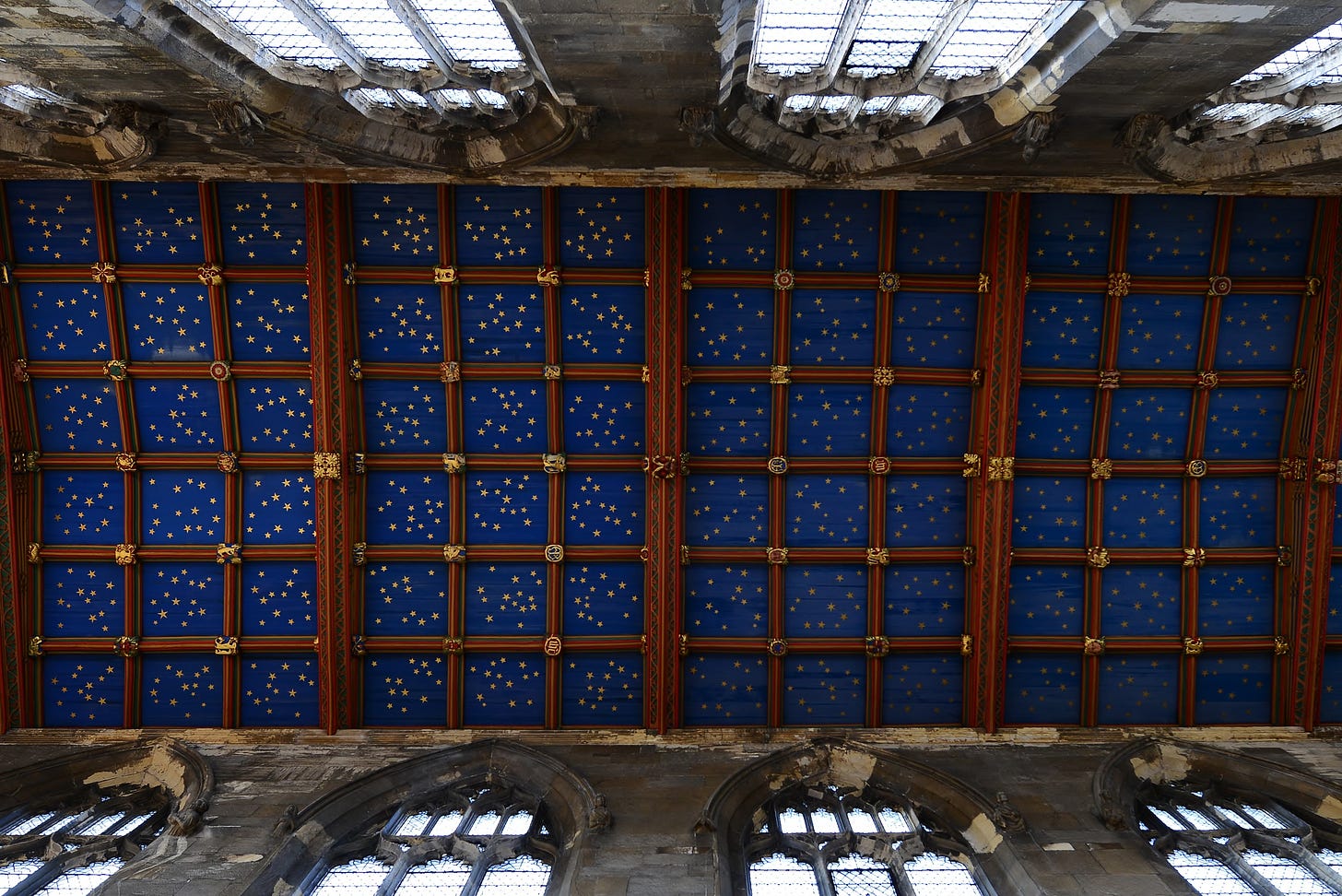 Photo of the ceiling of a medieval church from below, it is painted blue and covered in painted gold stars