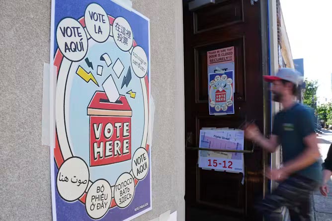 Man in T-shirt and baseball cap entered building with sign that says 'Vote Here.'