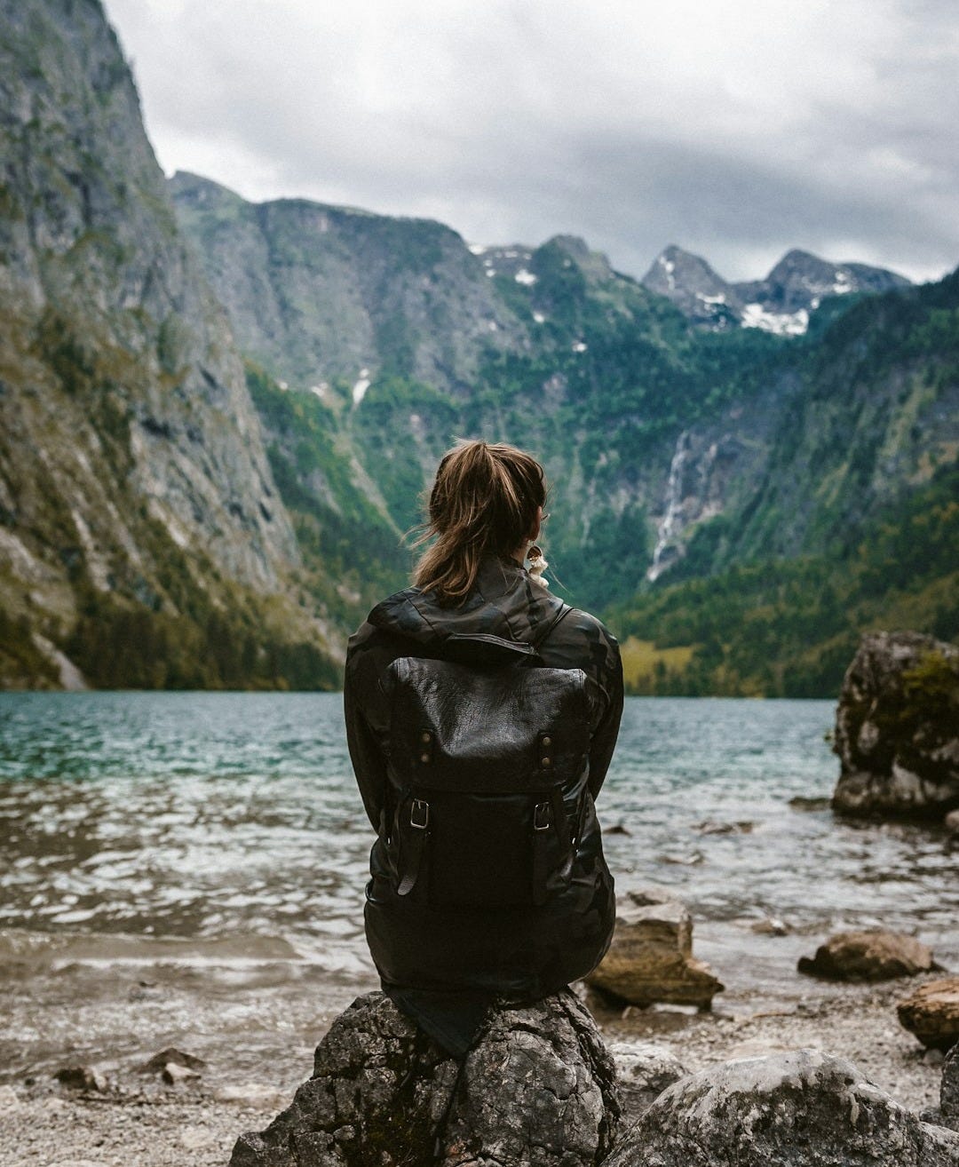 woman in black leather jacket standing on rock near body of water during daytime woman in black leather jacket standing on rock near body of water during daytime