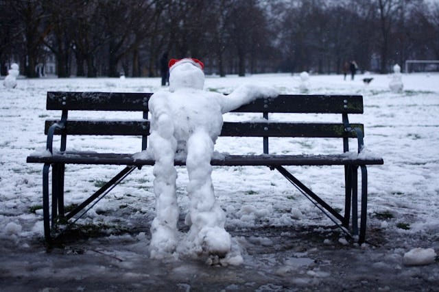 Image shows a melting snow person draped across a wooden park bench