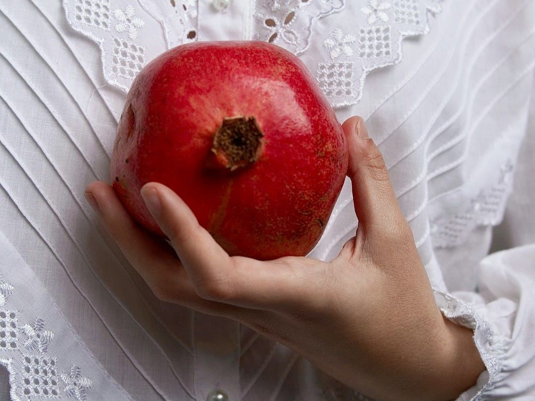 Hand holding a ripe pomegranate against white lace shirt