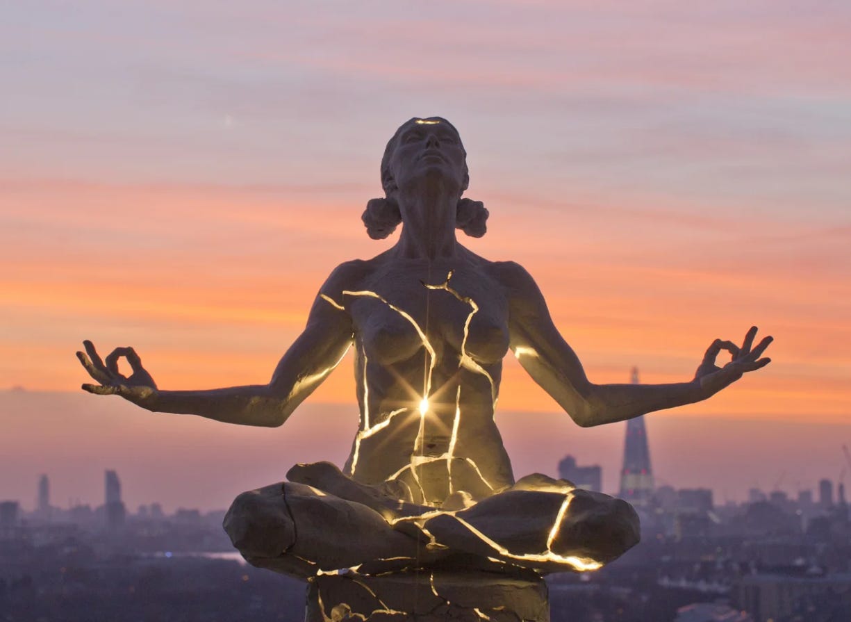 Paige Bradley’s sculpture of a woman in meditation with golden light streaming out from cracks in her body, against a sunset sky.  Paige Bradley’s sculpture of a woman in meditation with golden light streaming out from cracks in her body, against a sunset sky.