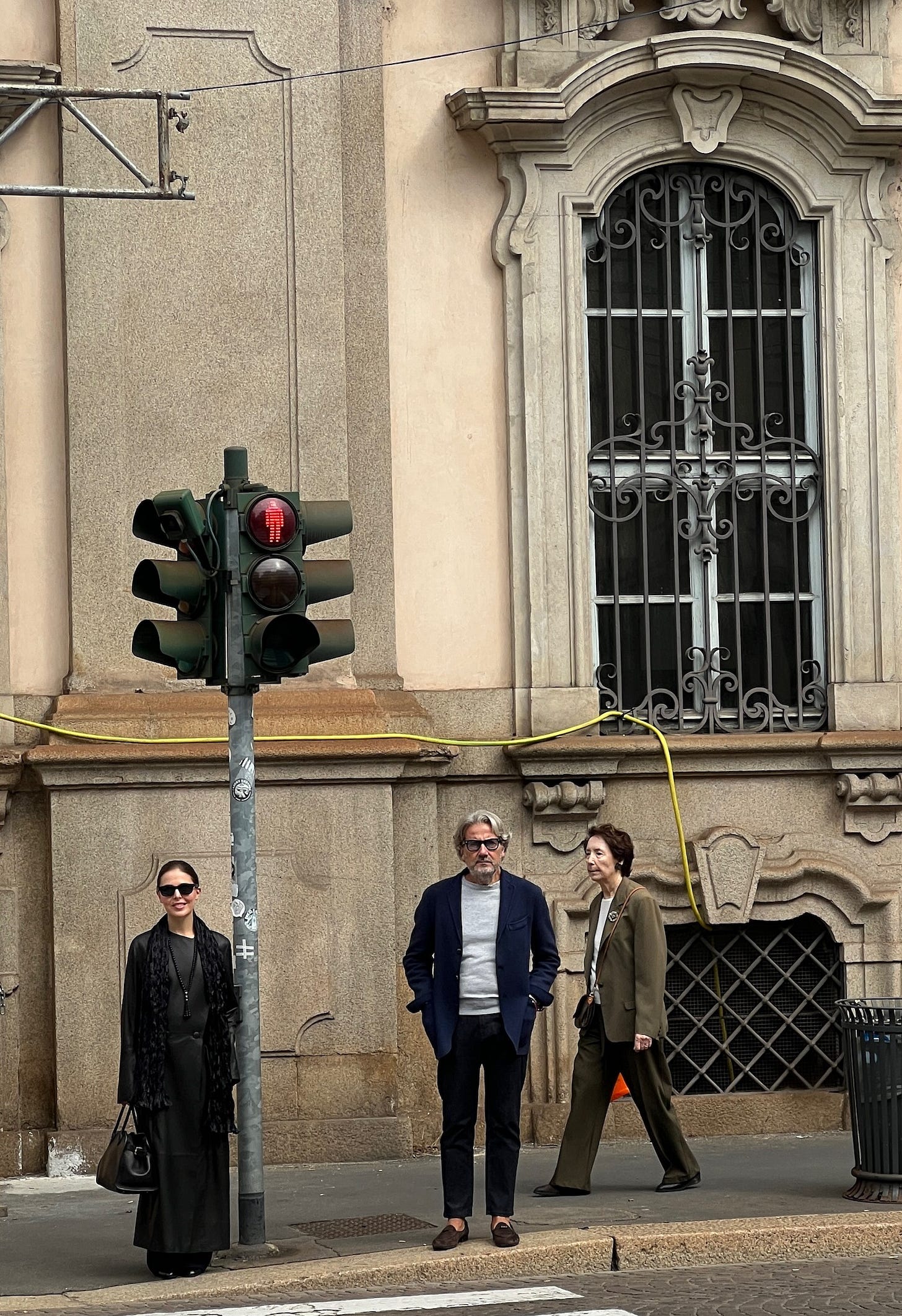 Three people waiting to cross the street in Milan, Italy.
