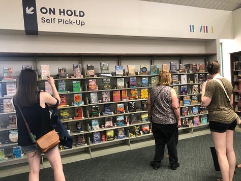 Adults and children in a public library borwworing, browsing, returning  books 