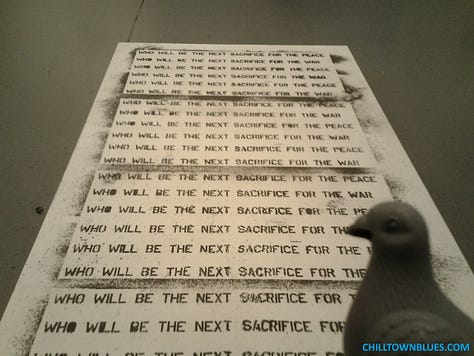 Chilltown Blues Photos: From top left to right, the Chilltown Blue Pigeon at a bird's eye view via a kind of widescreen, walking on cement path with a few petals strewn over it; pigeon in foreground at left, looking at Kei Ito's "Riddle of Peace and War," which alternates between the two lines: wwho will be the next sacrifice for the peace" and "who will be the next sacrifice for the war"; third in top row: Black and white image of pigeon head (figurine) in front of plant growth that looks like it's springing from its head coming from a gravely surface. Middle row, first from left: blue-gray pigeon figurine (with black-striped wing) adjacent to faded blue fire hydrant; center, bust of pigeon figurine, with small hole in neck, in front of nighttime landscape wherein a Christmas tree is across street, with green lights and a section along bottom missing as such; at right, silhouettle of pigeon figurine as two beige globe lanterns loom above in background on gray day; bottom left, black and white of pigeon figurine against large scattered leaves, all in grayscale;  cernter, pigeon figure looks in direction of tree as JC building looms in background; pigeon figurine in foreground as mid-ground has stop sign with "FU" grafitti on it, all in dark grayscale.