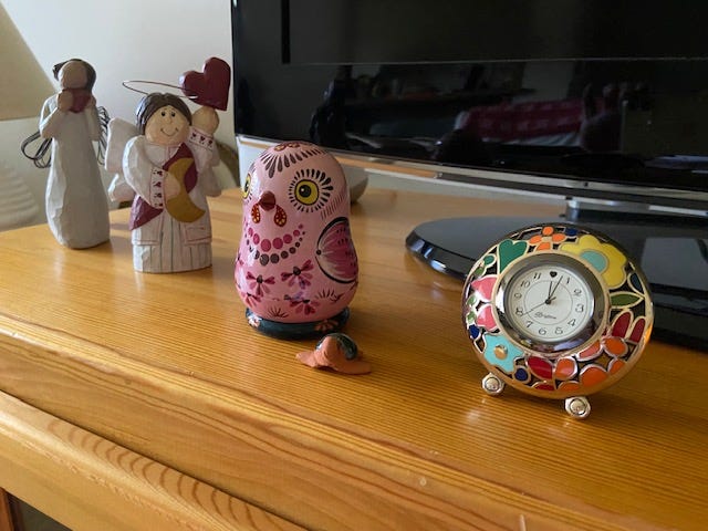 A desk clock with colorful designs rests next to a row of figurines: a small turtle, a pink bird, an angel with a red heart halo and an angel clutching a red heart.