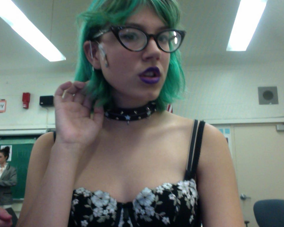 selfie of the author with bright green blue shoulder length hair and black cat eye glasses