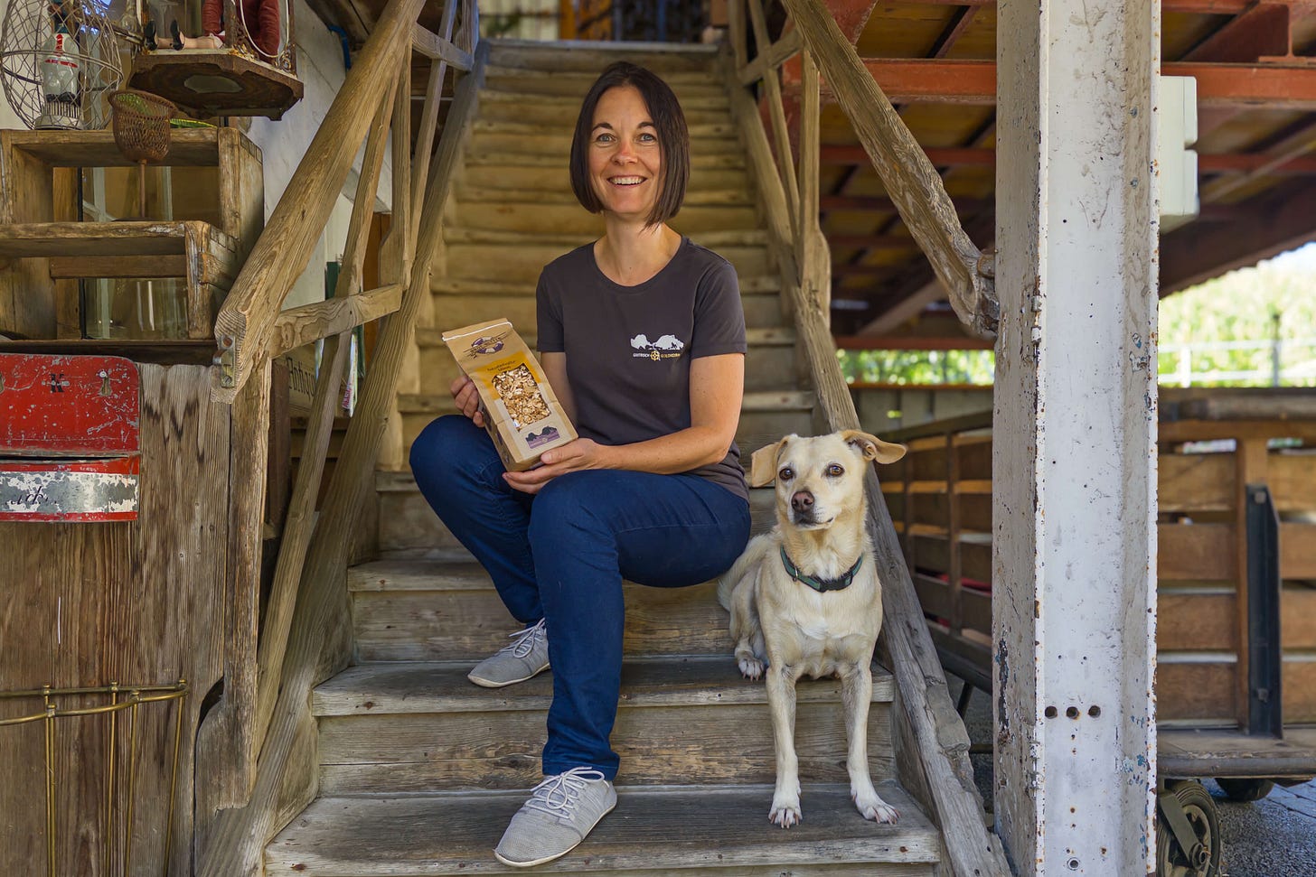 Carmen Bezençon sitzt mit ihrem Hund auf einer alten Holztreppe in der historischen Dittligmühle aus dem 19. Jahrhundert. Sie lächelt in die Kamera und hält eine Packung Fotzelschnitte-Müesli in den Händen. Carmen Bezençon sitzt mit ihrem Hund auf einer alten Holztreppe in der historischen Dittligmühle aus dem 19. Jahrhundert. Sie lächelt in die Kamera und hält eine Packung Fotzelschnitte-Müesli in den Händen.