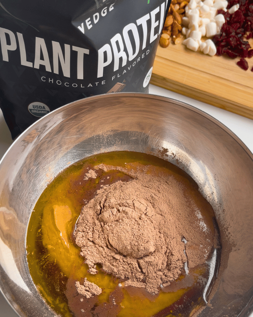 olive oil, chocolate protein powder, and other fudge ingredients in a metal bowl ready to be mixed